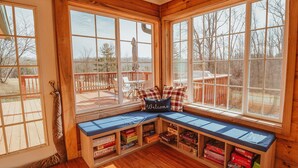 A cozy cabin with a built-in bench and shelves filled with board games, large windows offering a view of the deck and surrounding trees. - Log Cabin, Hot Tub, Fire Pit, Near Yellowwood (Nashville)