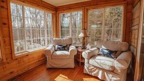 A cozy room with wooden walls and large windows, featuring two white armchairs with blue cushions and a small table with a lamp. - Log Cabin, Hot Tub, Fire Pit, Near Yellowwood (Nashville)