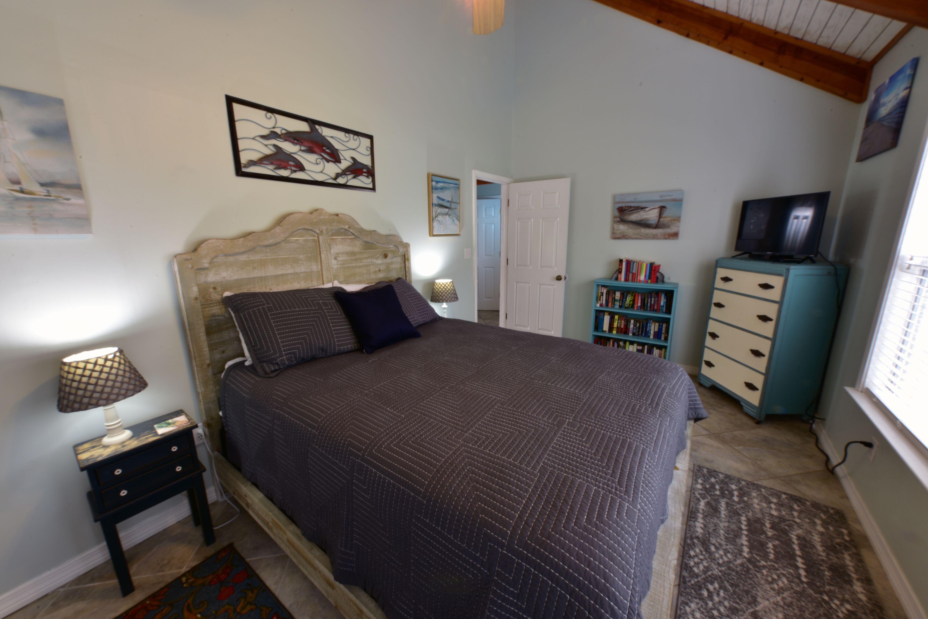 A bedroom with a large bed, a nightstand, a dresser, a TV, and a bookshelf.