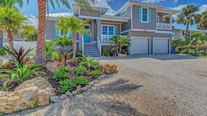 A two-story house with a covered patio, a driveway, and a well-maintained garden with palm trees and shrubs.
