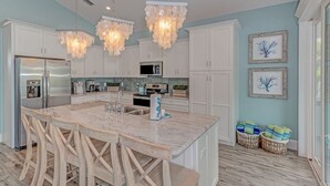 A modern kitchen with white cabinets, a marble island, and a stainless steel refrigerator.