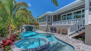 A swimming pool with a hot tub, surrounded by tropical plants and a stone waterfall feature.