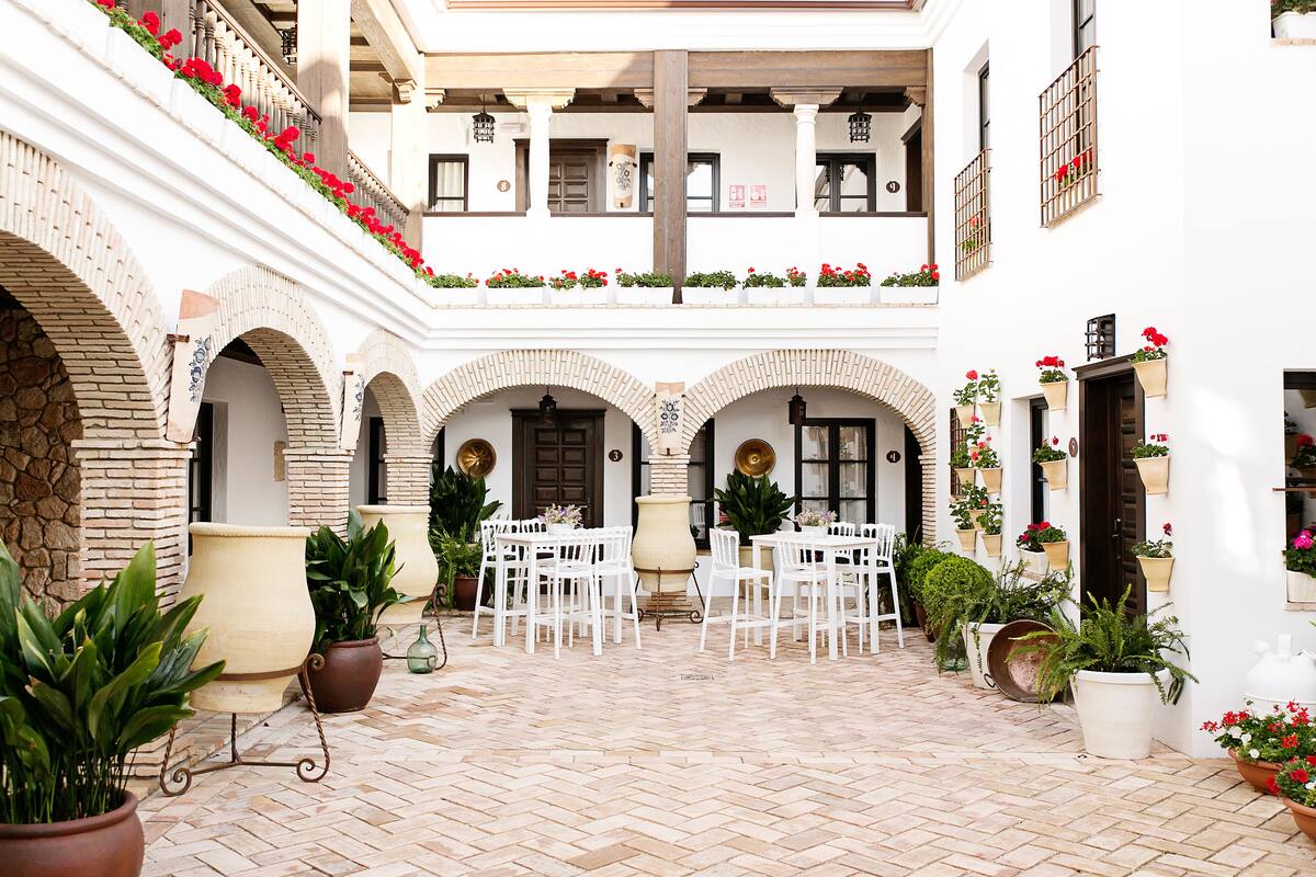 Une cour avec des chaises et des tables blanches, des plantes en pot et des fleurs rouges.