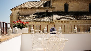 Una terraza con sillas y mesas de metal blanco, piso de baldosas y vista a un edificio histórico con campanario.