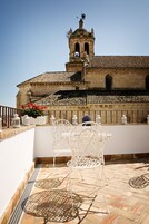 A terrace with white metal chairs and tables, a tiled floor, and a view of a historic building with a bell tower.