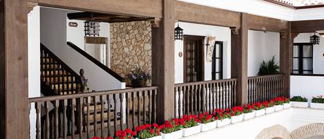 A covered outdoor area with a wooden railing, red flowers, and a stone wall.