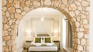 Un dormitorio con un arco de piedra, una cama con dosel, lámparas de noche y una mesita.