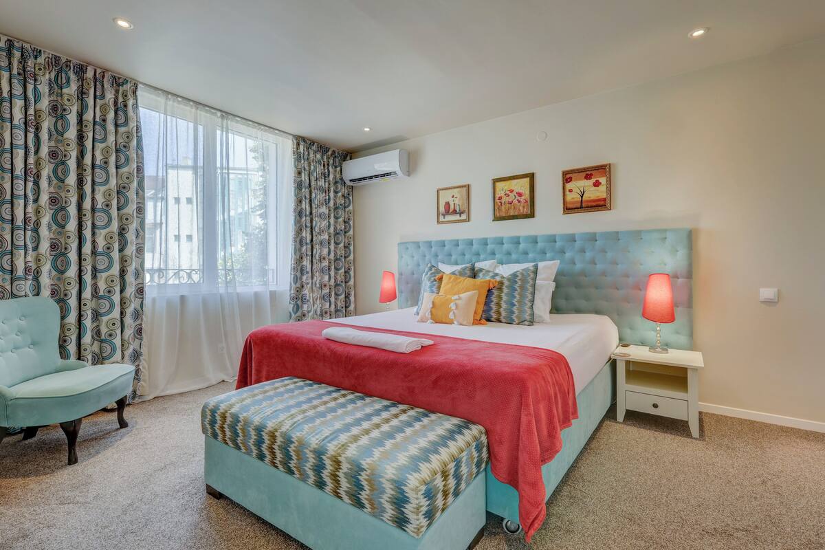 A bedroom with a large bed, a chair, a bench, and a nightstand with a lamp.
