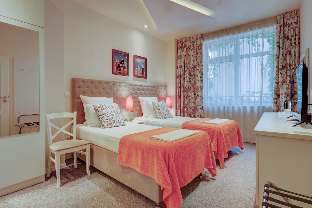 A hotel room with two beds, a desk, a chair, and a TV.