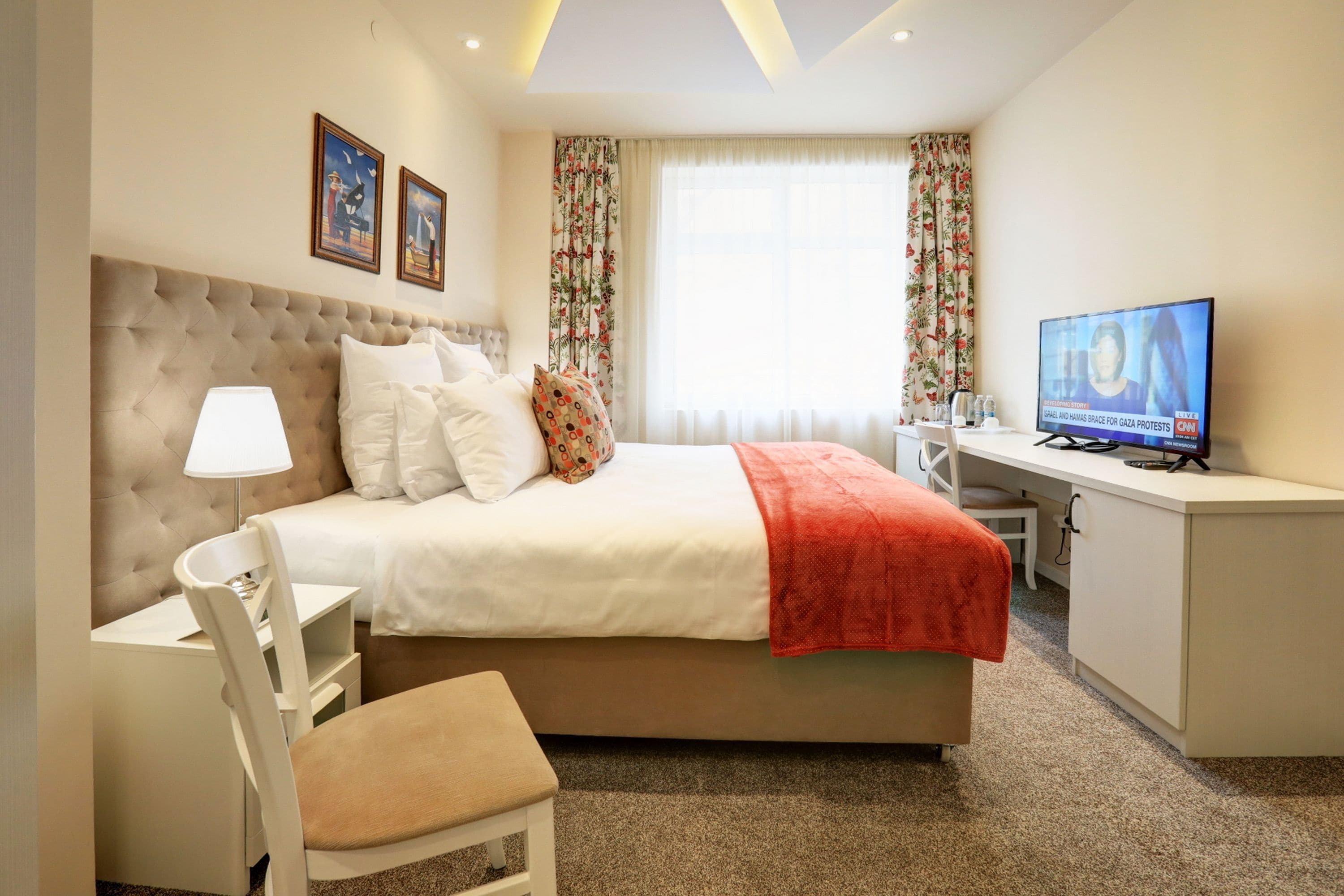 A hotel room with a bed, a desk, a chair, a TV, and a window with curtains.