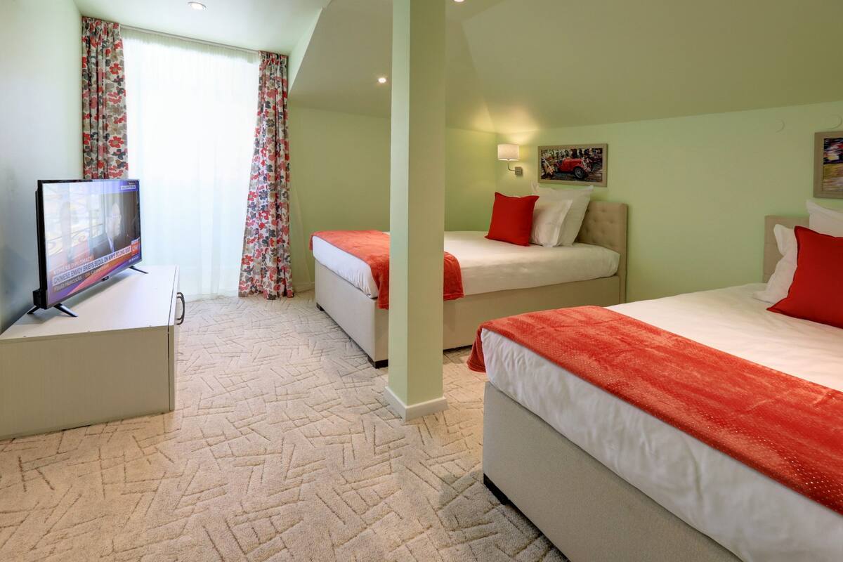 A hotel room with two beds, a television, and a window with curtains.