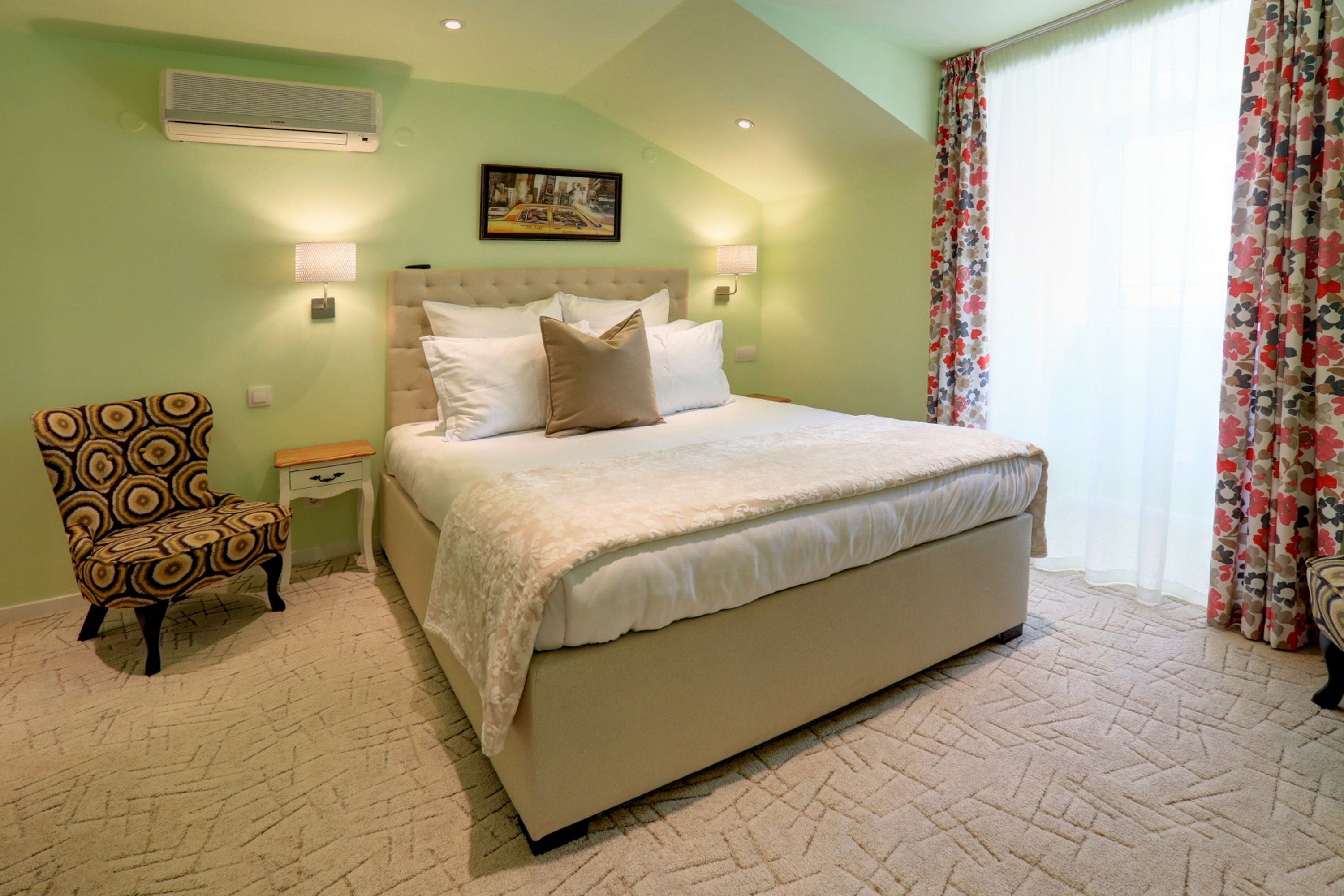 A bedroom with a large bed, a nightstand, a chair, and a wall-mounted air conditioner.