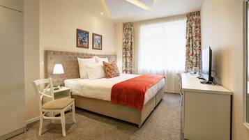 A hotel room with a bed, a desk, a chair, a television, and a window with curtains.