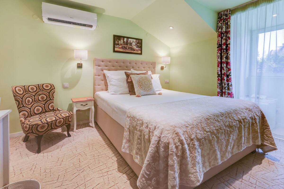 A bedroom with a large bed, a chair, a nightstand, and a wall-mounted air conditioner.