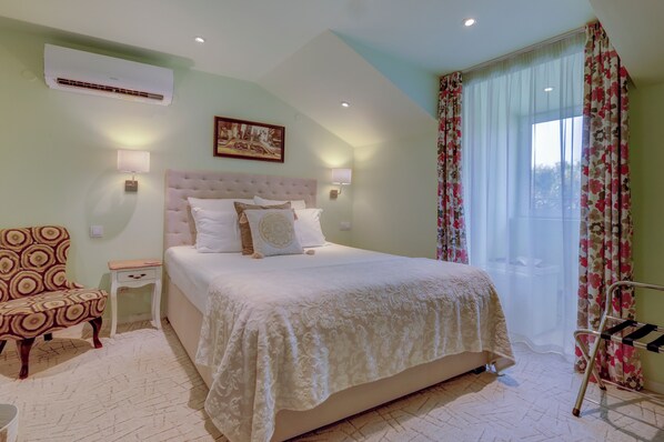 Un dormitorio con una cama grande, una mesita de noche, una silla, un equipo de aire acondicionado y una ventana con cortinas.