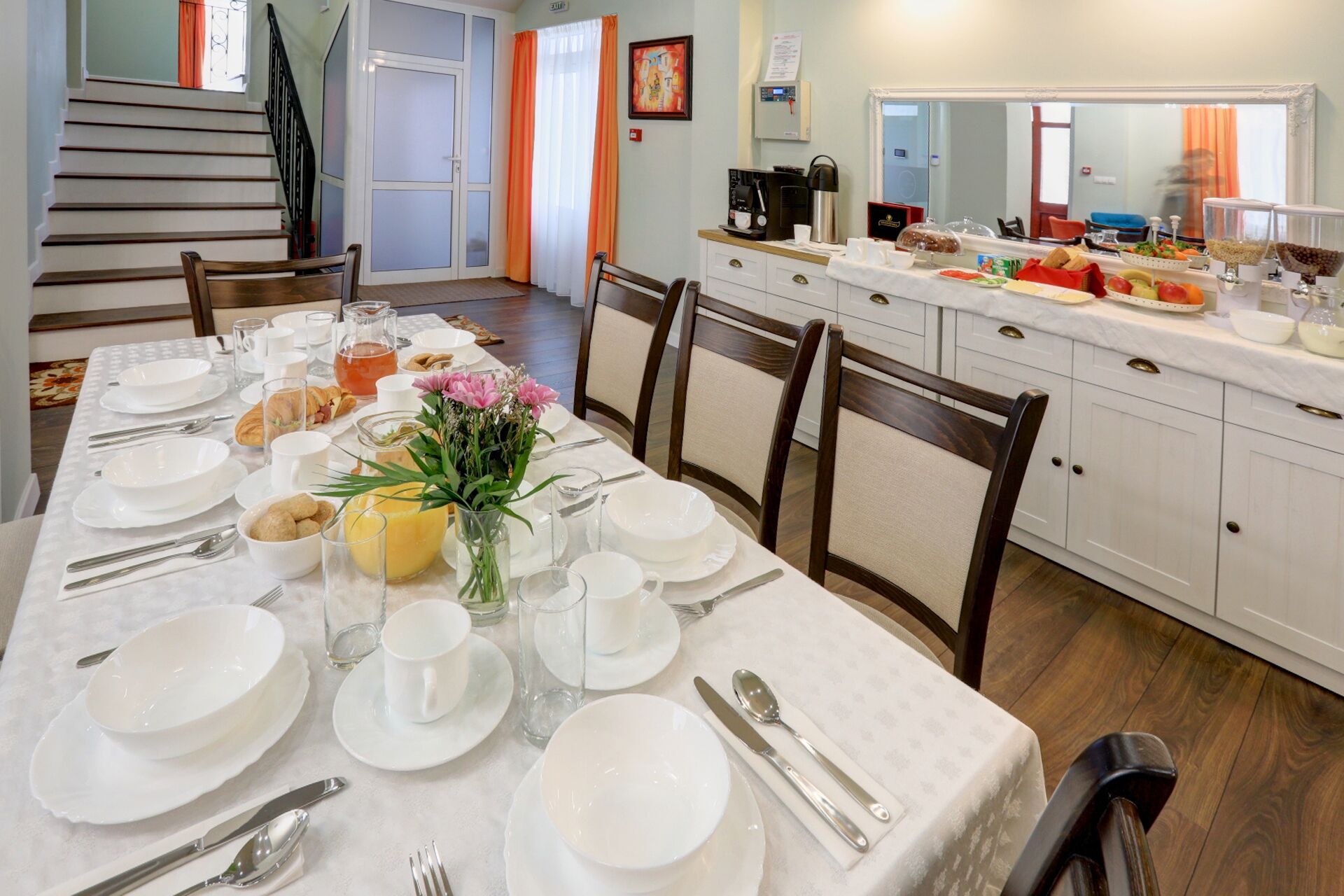Un comedor con una mesa dispuesta para cuatro personas, con platos, cubiertos y un florero.