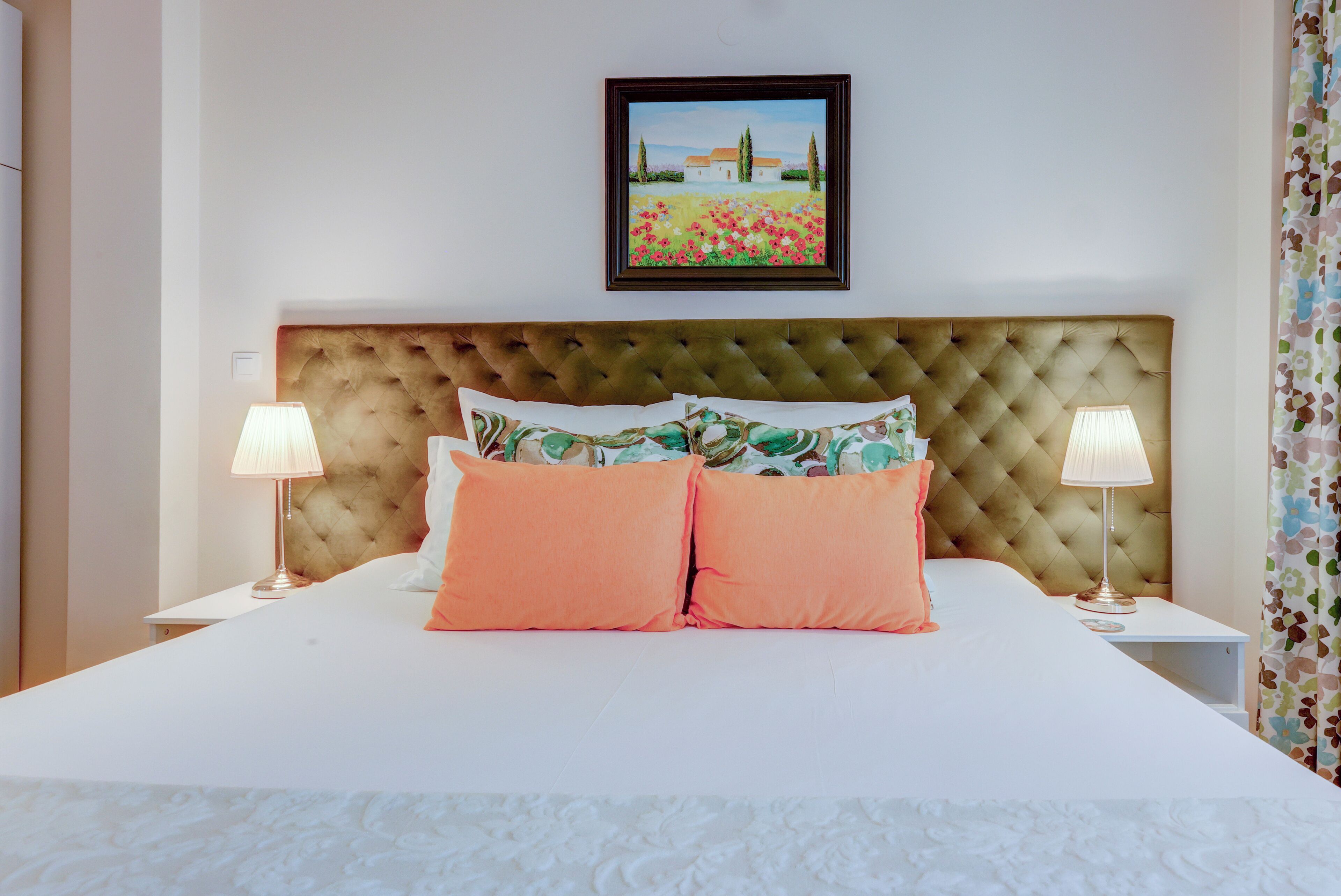 A neatly made bed with a tufted headboard, two bedside lamps, and a framed painting above.