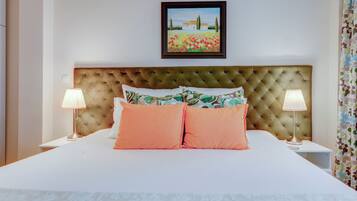 A neatly made bed with a tufted headboard, two bedside lamps, and a framed painting above.
