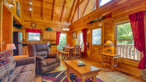 A cozy cabin interior with a wooden dining table, leather sofa, and a kitchen area with a refrigerator and cabinets. - Charming Cabin with Private Hot Tub & Pool Table (Sevierville)