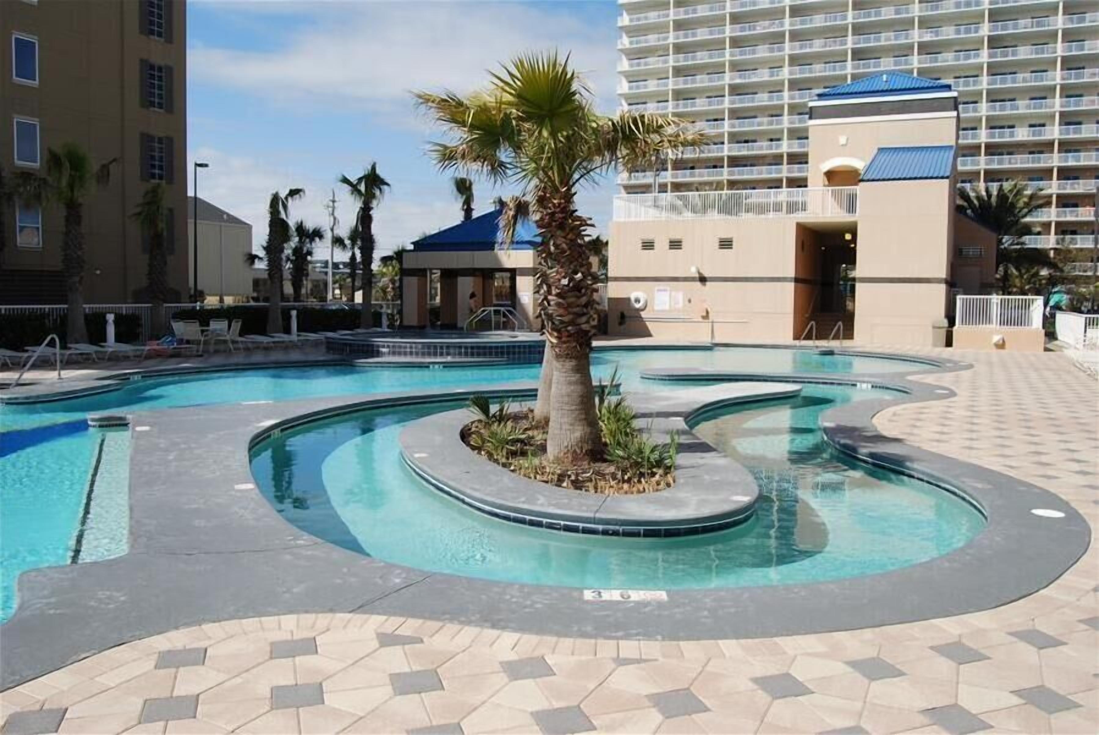 Ein Swimmingpool mit einer zentralen Palme, umgeben von einer gefliesten Terrasse.