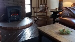 A cozy living room with a fireplace, a wooden chair, a leather couch, and a table with a candle. - Adirondack Rustic 2 Story- 10 ACRES-SKI, SKI, SKI! (Warrensburg)