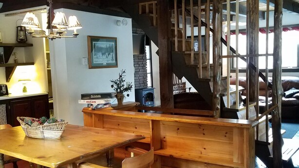 A rustic interior with a wooden dining table, benches, and a staircase with a wooden railing. - Adirondack Rustic 2 Story- 10 ACRES-SKI, SKI, SKI! (Warrensburg)