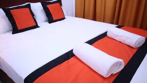 A neatly made bed with white and orange bedding, two pillows, and two rolled towels. - Lakeside Hybrid Villa (Bandaragama)
