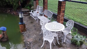 A patio with white metal chairs and a table, surrounded by a brick wall and a chain-link fence. - Lakeside Hybrid Villa (Bandaragama)