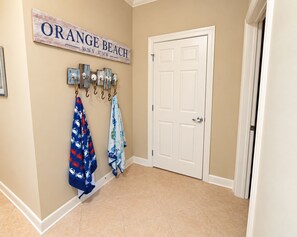 A hallway with a white door, a sign reading 'ORANGE BEACH,' and two towels hanging on hooks. - Spacious Gulf-Front 4BR Condo | Sleeps 10 | Huge Balcony | Indoor & Outdoor Pools (Orange Beach)