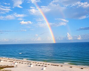 Une plage avec un arc-en-ciel se déployant au-dessus de l’océan, du sable blanc et une jetée en bois.