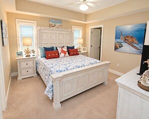 A bedroom with a large bed, two bedside tables, a ceiling fan, and a painting of a turtle on the wall. - Spacious Gulf-Front 4BR Condo | Sleeps 10 | Huge Balcony | Indoor & Outdoor Pools (Orange Beach)