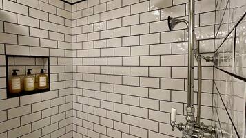 A bathroom with white subway tiles, a shower with a handheld showerhead, and a shelf with three bottles.