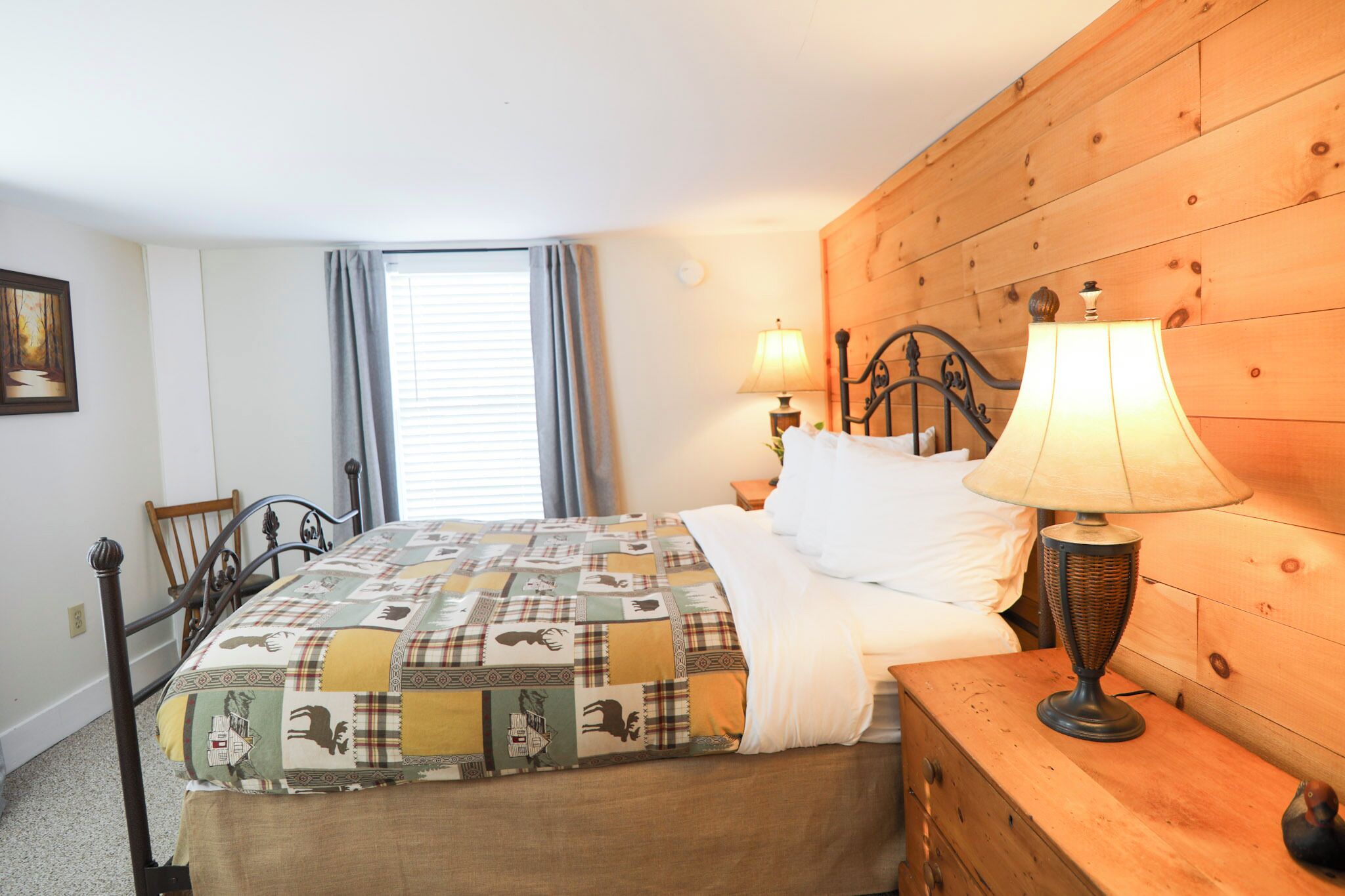 Une chambre à coucher avec une tête de lit en bois, une couvre-lit matelassée, deux lampes de chevet, une commode en bois et une fenêtre avec des rideaux.