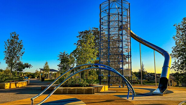 A playground with a slide, a climbing structure, and a curved metal frame.
