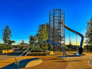 Une aire de jeux avec un toboggan, une structure d’escalade et une armature métallique incurvée.
