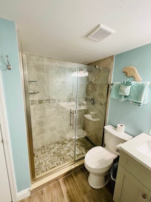 Een badkamer met een douche met glazen wand, een wit toilet, een wastafel en een handdoekrek met een handdoekhouder in de vorm van een dolfijn.