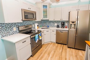 A modern kitchen with stainless steel appliances, a tiled backsplash, and light wood flooring.