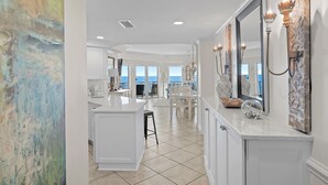 Une cuisine spacieuse dotée d’un grand îlot central, de meubles blancs et offrant une vue sur l’extérieur.