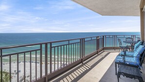 Un balcon avec vue sur l’océan, un coin salon avec des coussins à rayures bleues, ainsi qu’une table et des chaises.