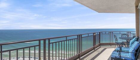 A balcony with a view of the ocean, a seating area with blue-striped cushions, and a table and chairs.