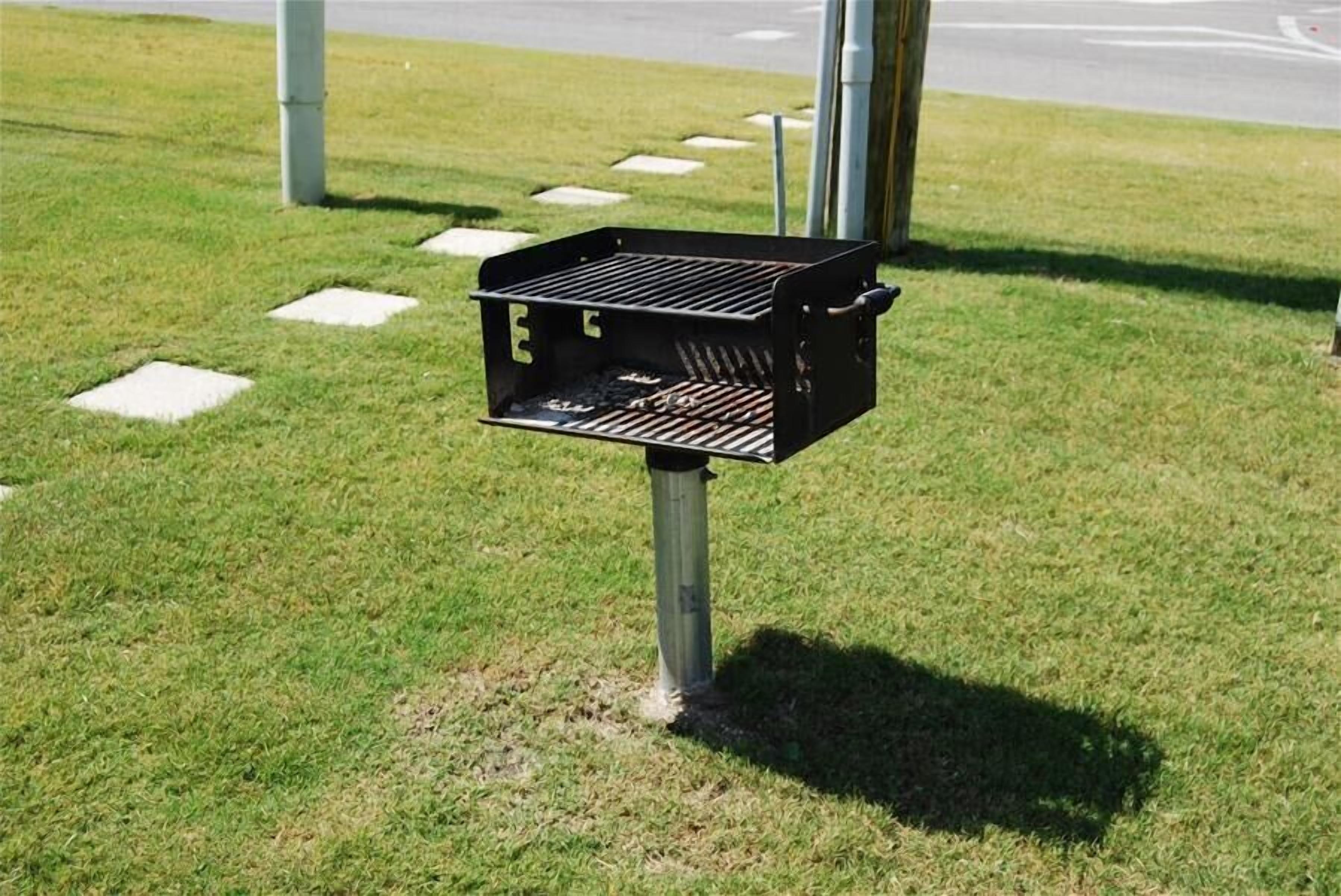 Un barbecue portable installé sur une pelouse, avec un poteau en métal.