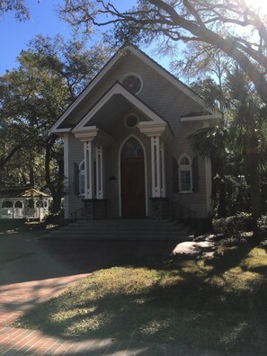 A two-story building with a gabled roof, a central entrance with a door, and a small porch with columns.