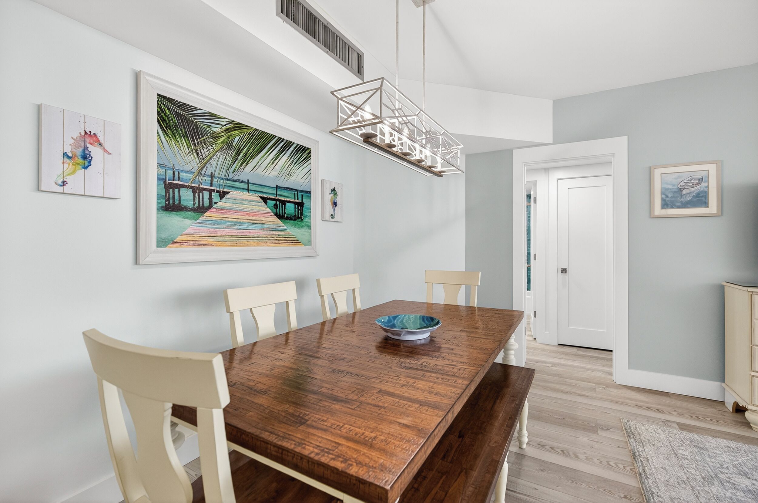 A dining area with a wooden table, white chairs, a hanging light fixture, and artwork on the walls.