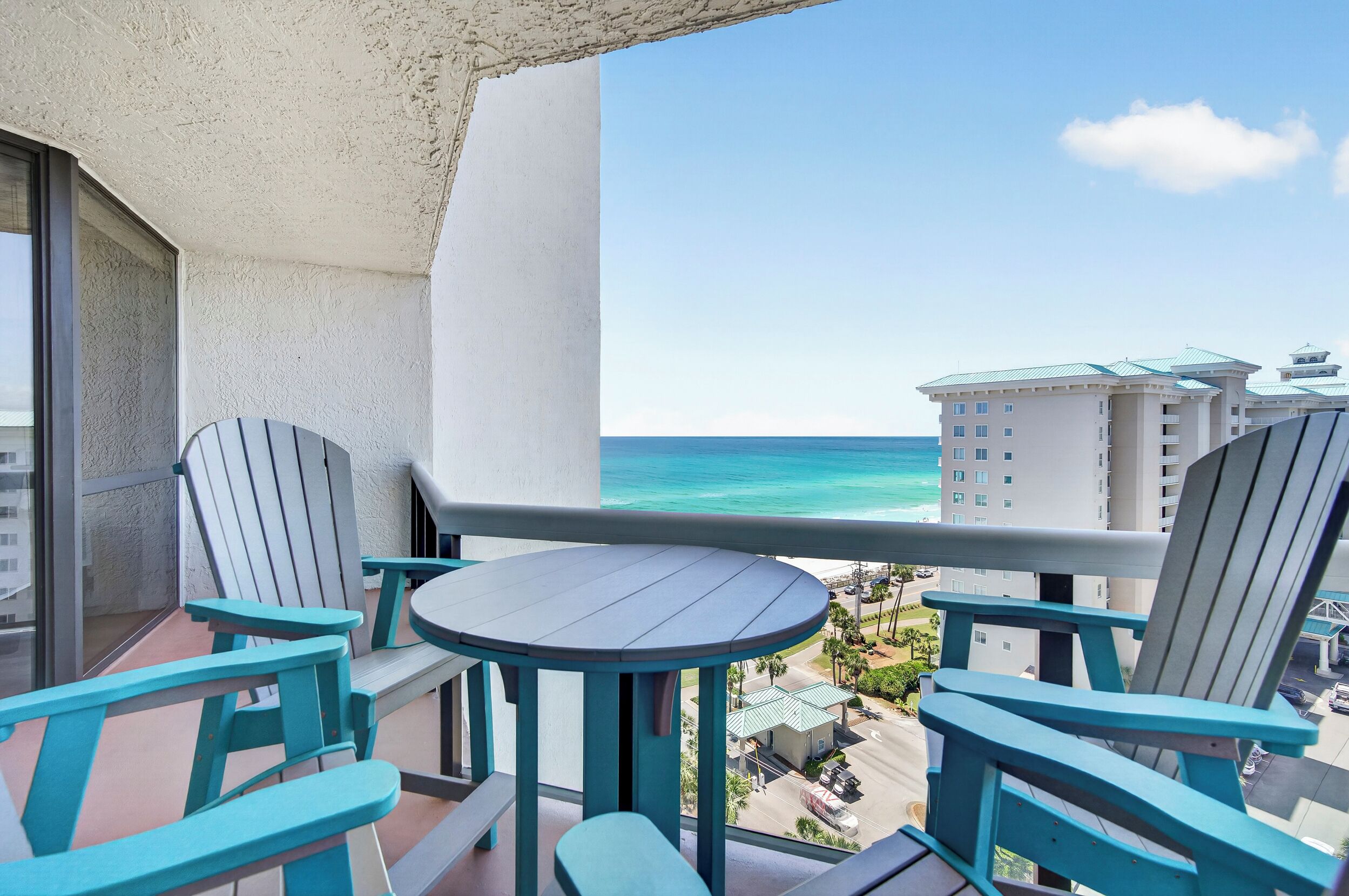 Un balcon avec deux chaises et une table, donnant sur une plage et des immeubles.