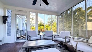 Ein Wintergarten mit Deckenventilator, großen Fenstern und einer Sitzecke mit Tisch.