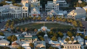 An aerial view of a coastal residential area with multiple houses, a central gazebo, and a beach in the foreground.