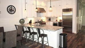 A modern kitchen with white cabinetry, a stainless steel refrigerator, and pendant lighting.