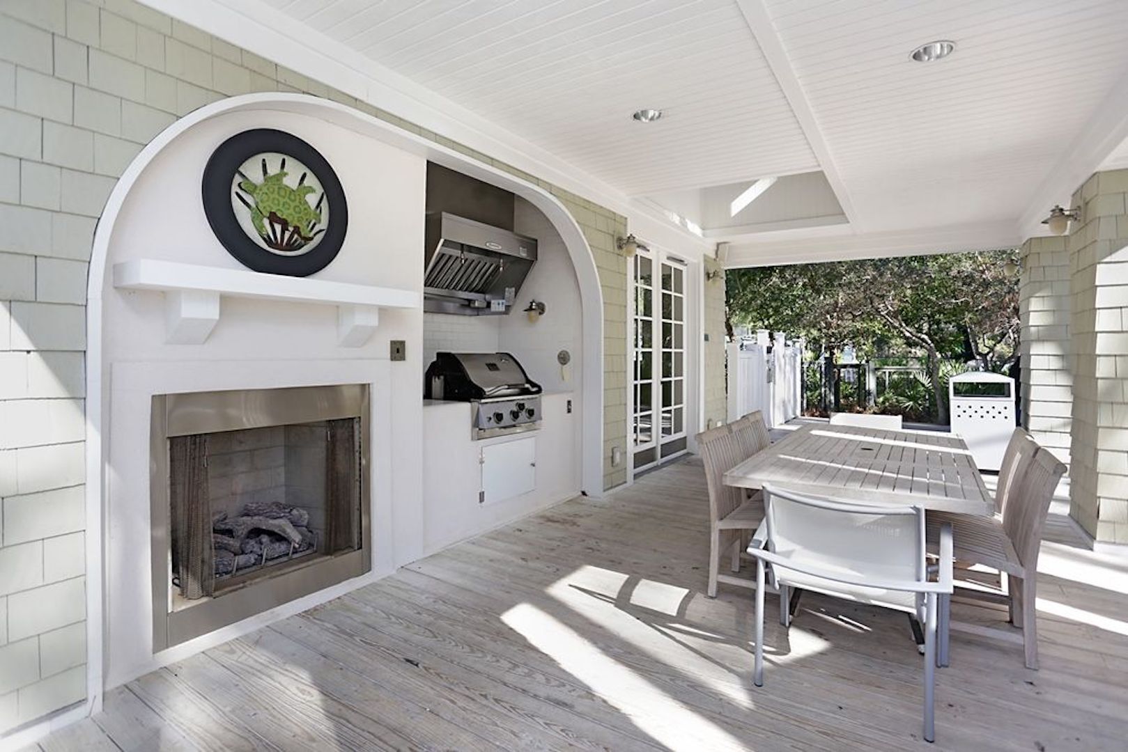 A covered patio area with a grill, a fireplace, and a dining table with chairs.