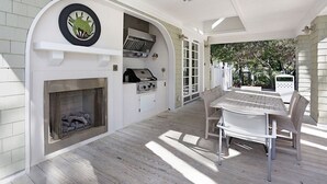 A covered patio area with a grill, a fireplace, and a dining table with chairs.