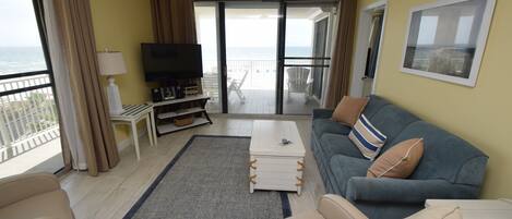 A living room with a sofa, a coffee table, a TV, and a balcony with a view.